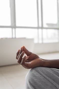 Person practicing meditation indoors with a focus on hand gesture for relaxation and mindfulness.