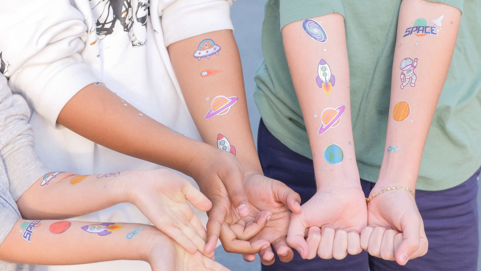 Children showing off space-themed temporary tattoos featuring rockets and planets. — free online jigsaw puzzle on JigsawPuzzlesFreeOnline.org