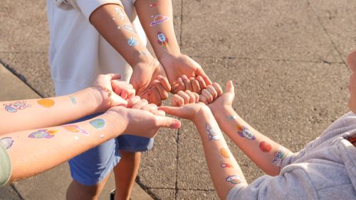 Free Children displaying space-themed temporary tattoos on their arms outdoors. Stock Photo