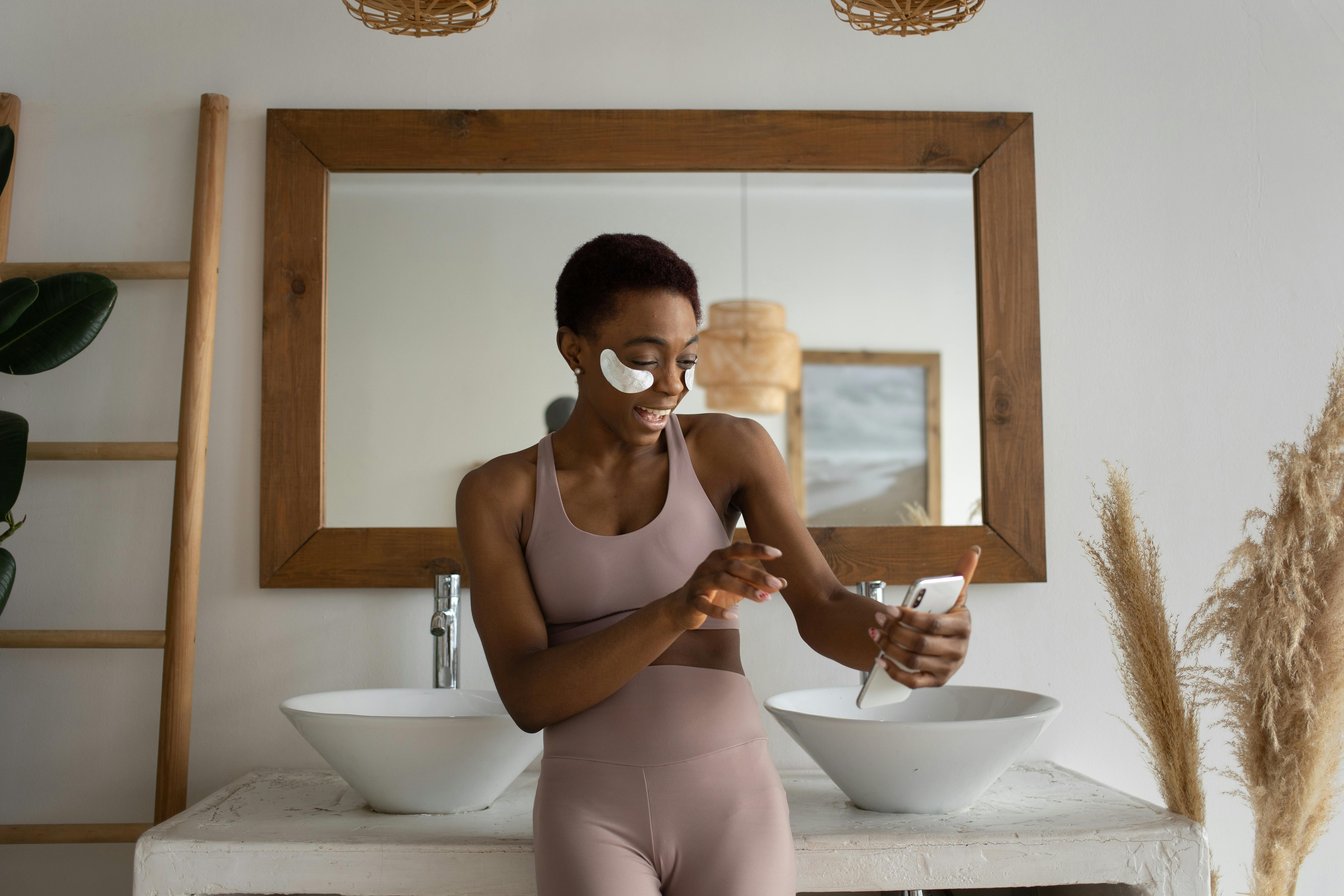 woman standing in a bathroom with eye patches on and talking to somebody through a video call