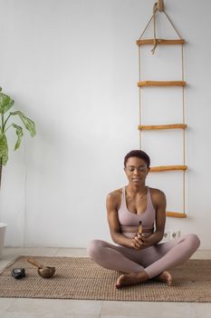 African American woman practicing meditation indoors with a singing bowl, promoting wellness.