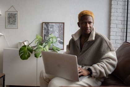 Black man working on a laptop in a cozy indoor setting with plant decor — photo by Katrin Bolovtsova on Pexels