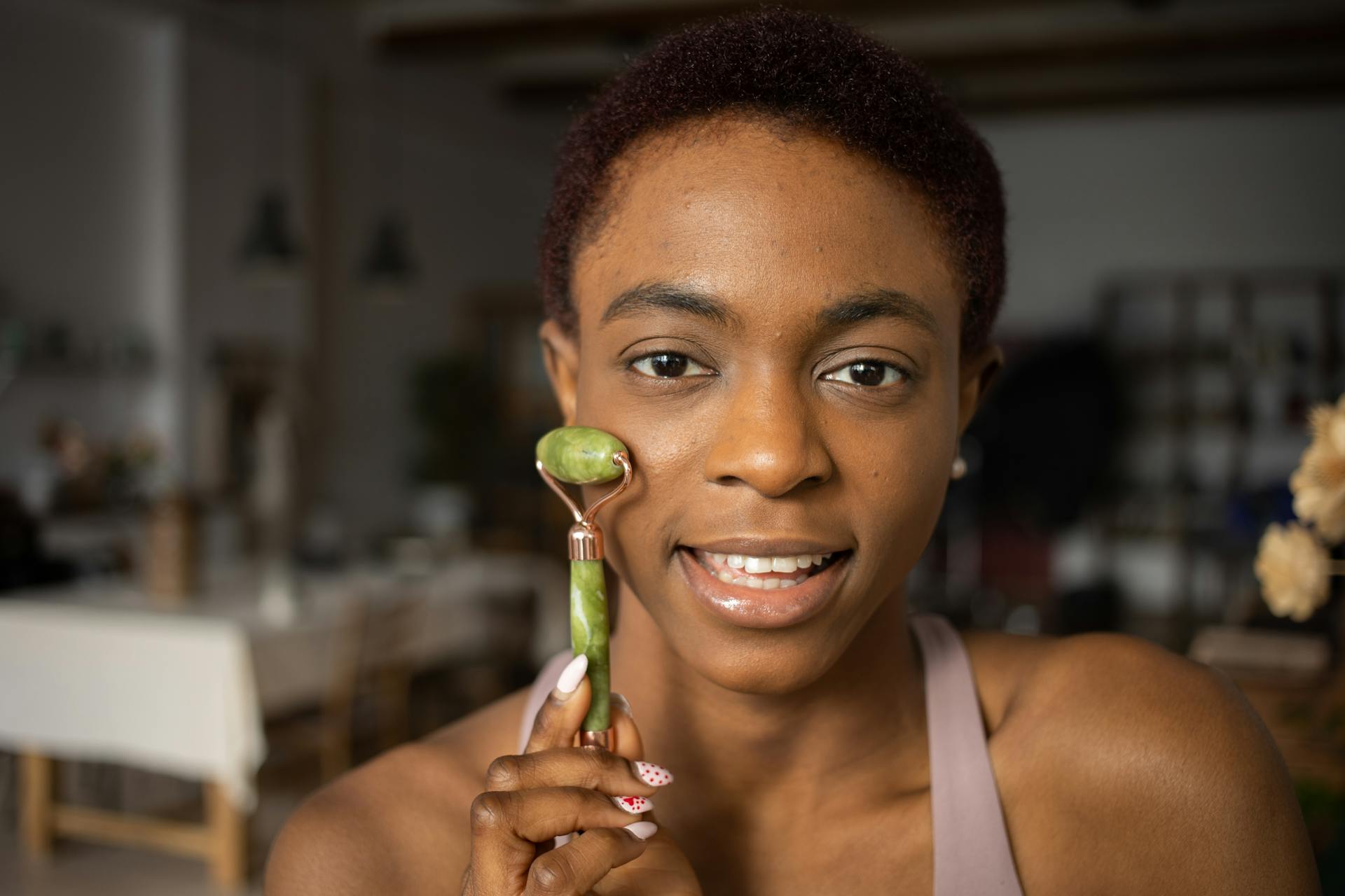 Close-up of a woman using a jade roller for her skincare routine indoors.