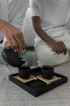 A calming indoor tea ceremony featuring a black teapot pouring into two black cups on a tray.
