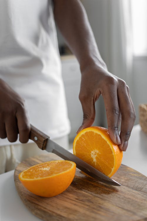 Person Slicing Orange on Wooden Chopping Board