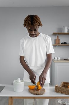 Young man preparing fresh orange slices on a wooden board in a contemporary kitchen.
