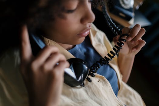 Close-up of a young woman holding a retro rotary phone, engaging in a conversation indoors.