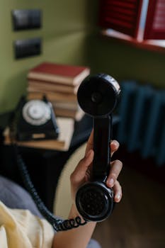 Close-up of a hand holding a vintage rotary phone handset in a cozy room setting.