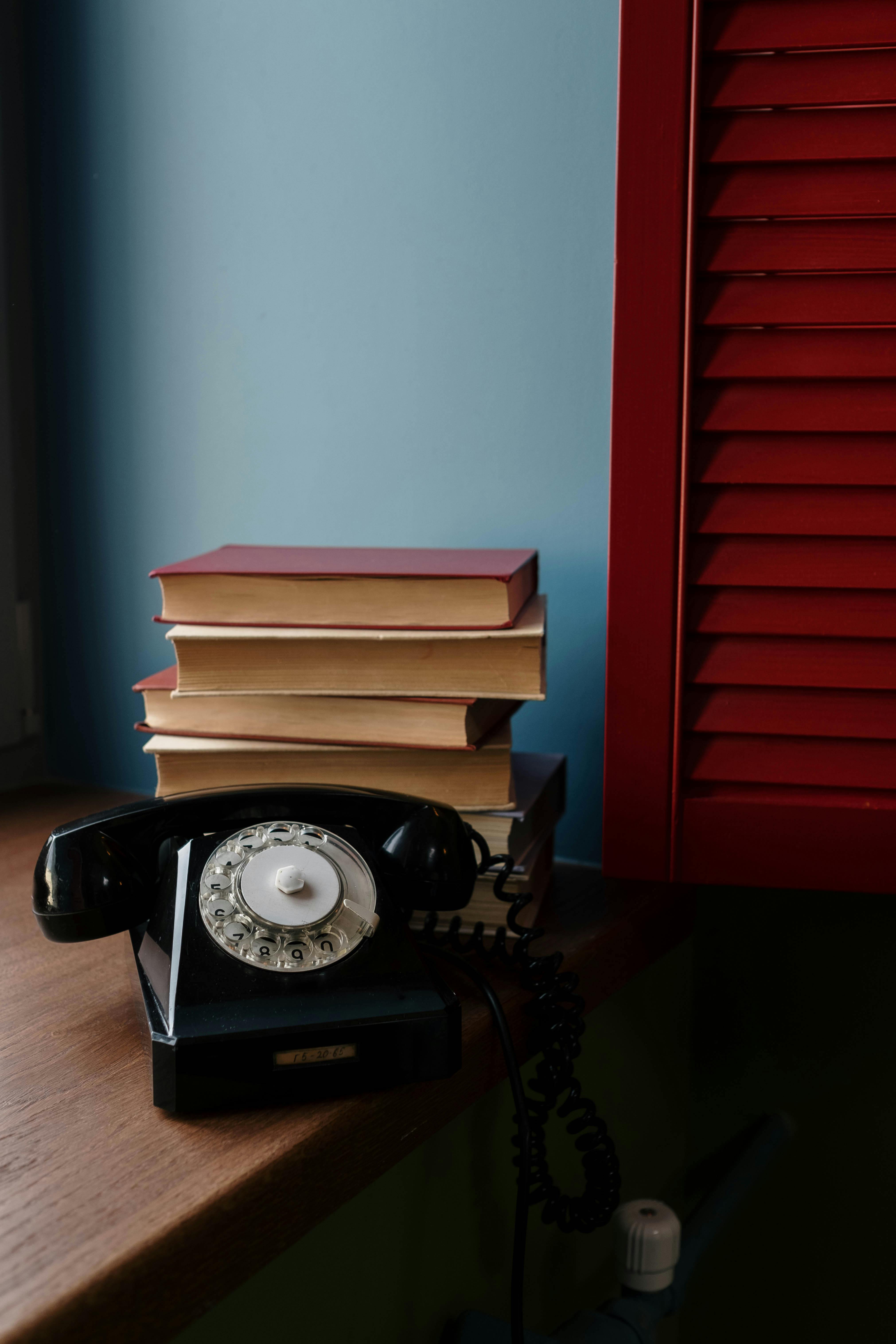 A nostalgic scene with a vintage rotary phone and stack of books by a window.