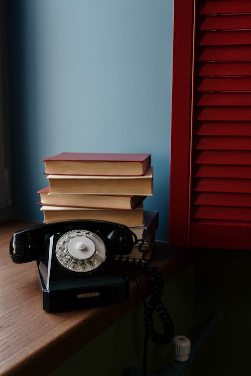 A Black Rotary Telephone beside a Stack of Books