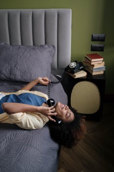 Woman lying on bed with retro phone, enjoying a call in cozy setting.