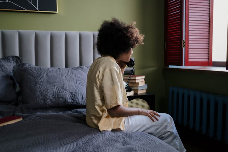 Young Woman Sitting On Bedside Talking On Phone 