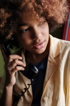 Young woman with afro hair holding a vintage telephone indoors.