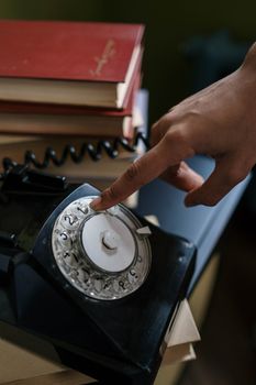 Close-up of a hand dialing a classic black rotary phone with books in the background.
