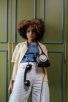 A young black woman with afro hair posing indoors with a vintage rotary phone.