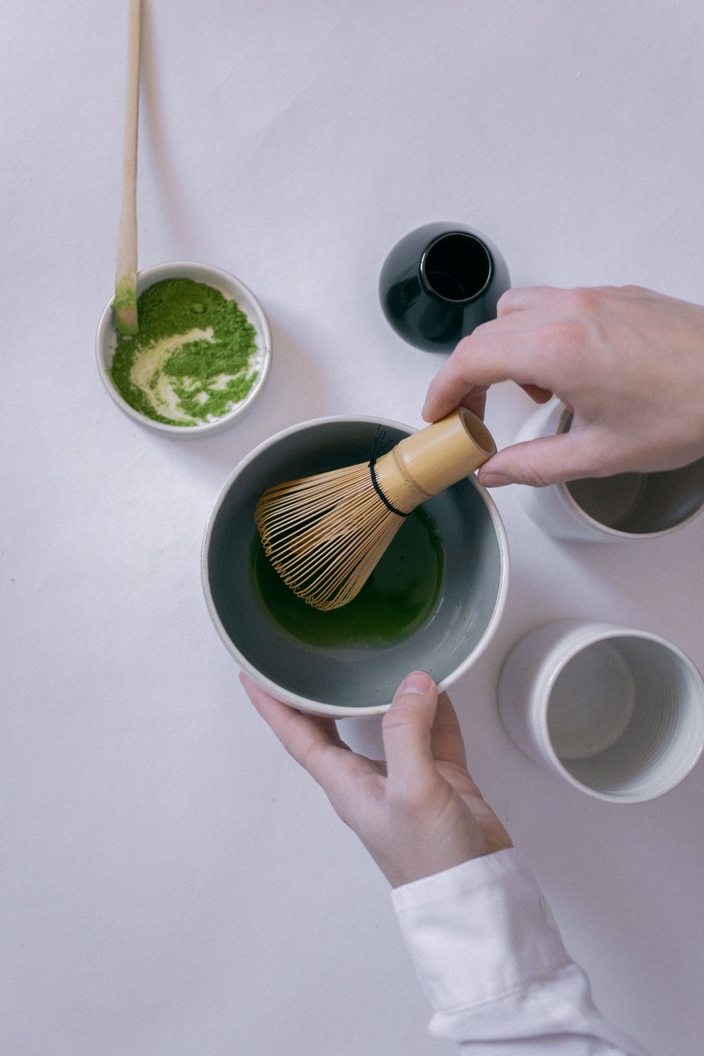 Hands preparing matcha tea with a bamboo whisk in a ceramic bowl