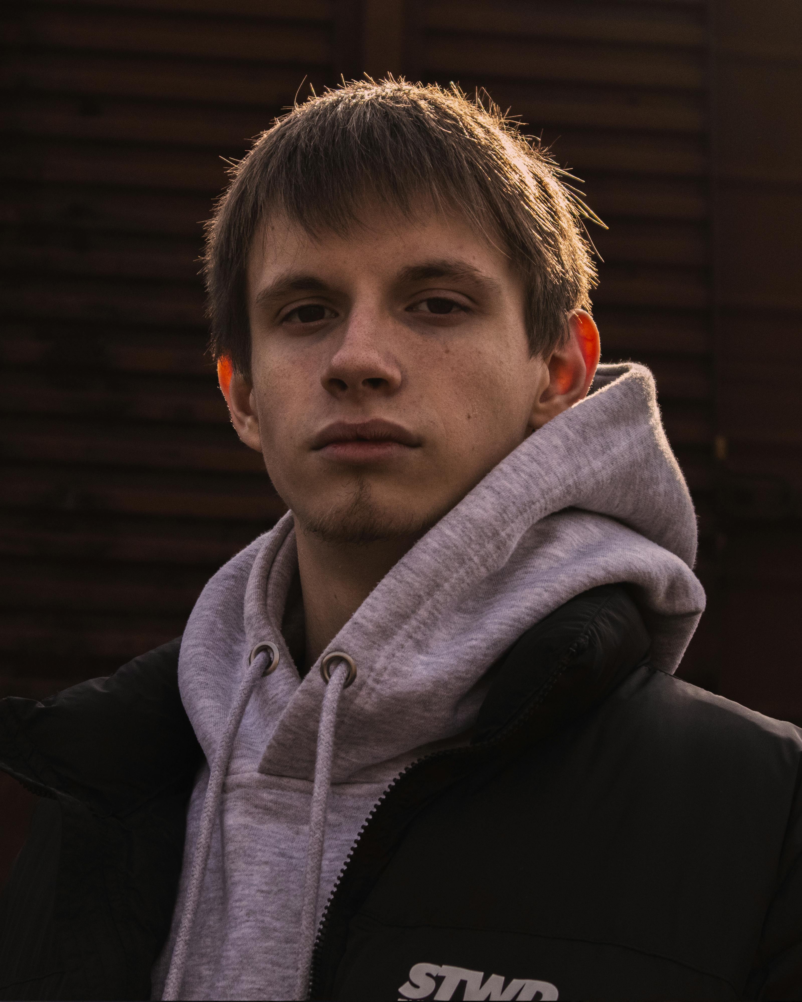 Moody portrait of a young man wearing a hoodie and jacket, captured in natural lighting.
