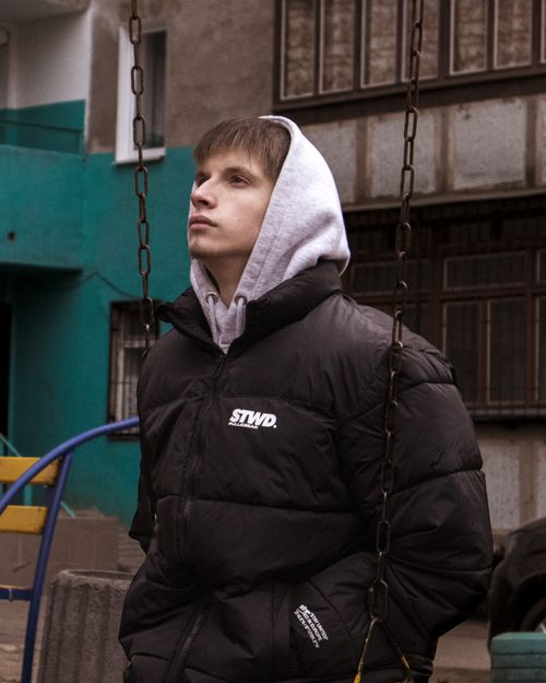 Free Young man in a hoodie and jacket sitting on a swing in an urban setting in Odesa, Ukraine. Stock Photo