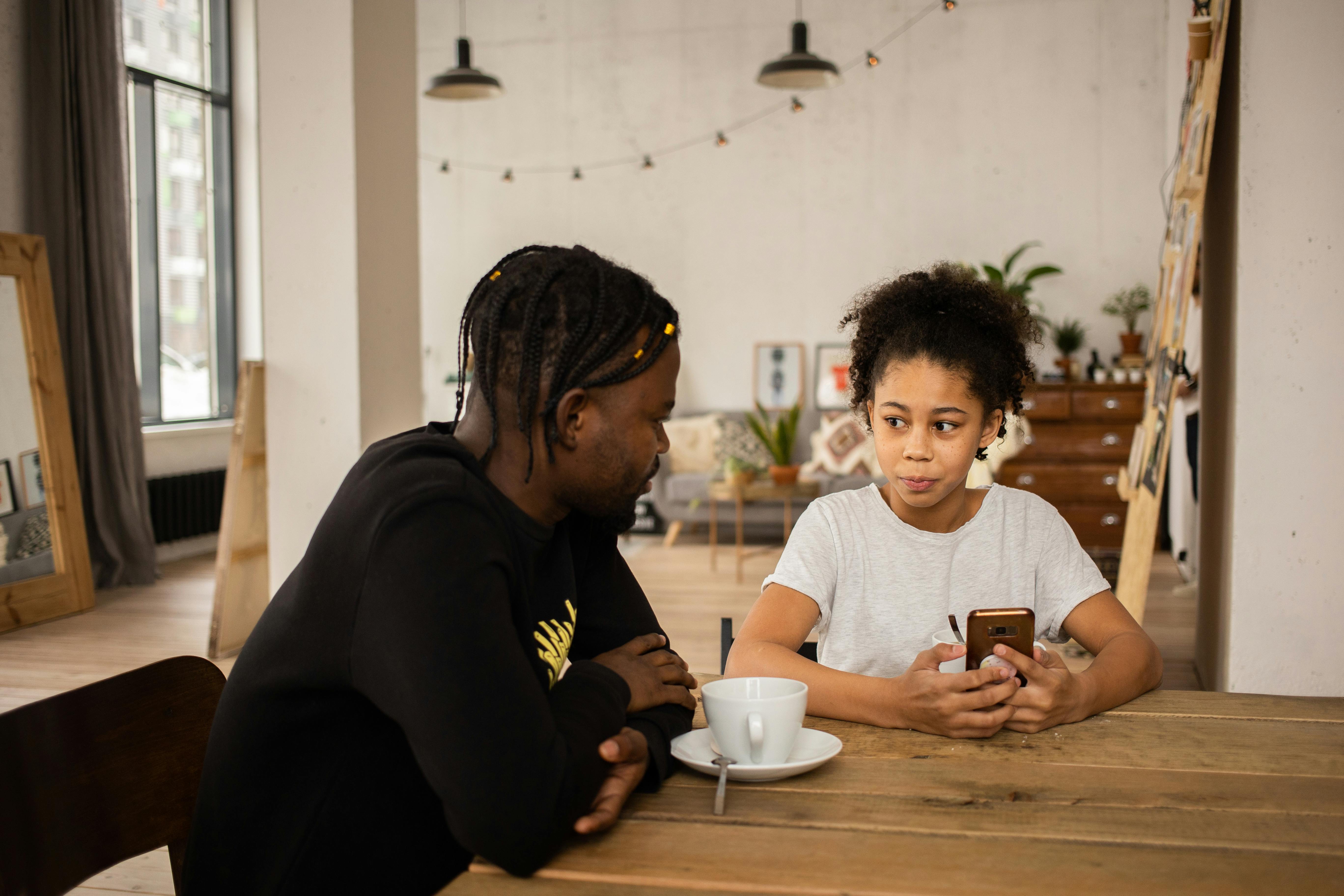 black father talking to daughter using smartphone