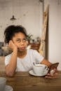 Annoyed black girl surfing smartphone at table with coffee