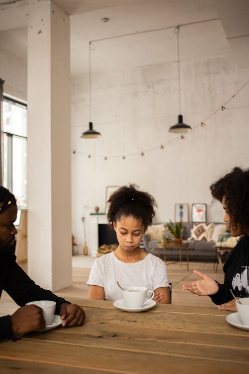 Free Dissatisfied African American mother gesticulating while scolding upset daughter sitting at table near crop father Stock Photo