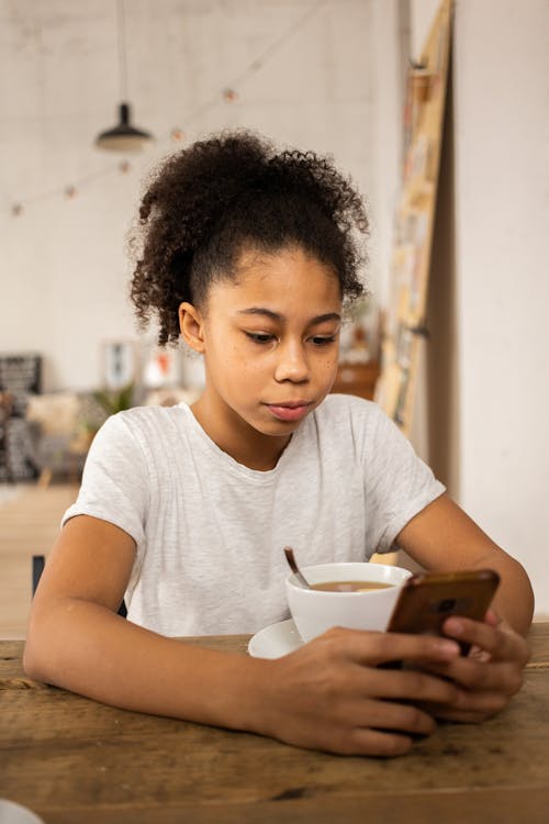 Black girl using smartphone while drinking coffee