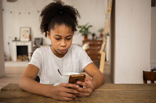 Black girl surfing Internet on smartphone at table with coffee