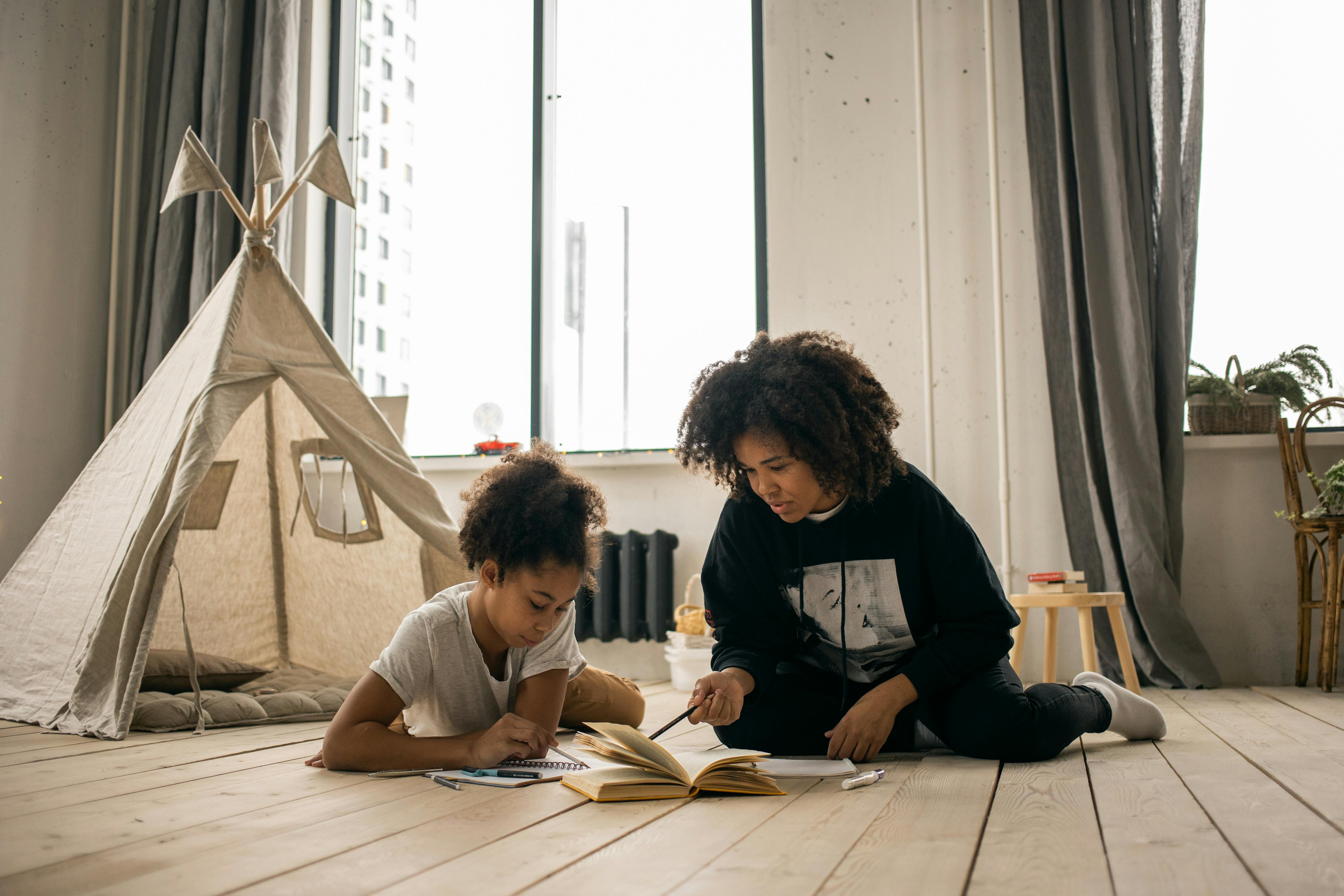 black mother pointing in book while doing task with daughter