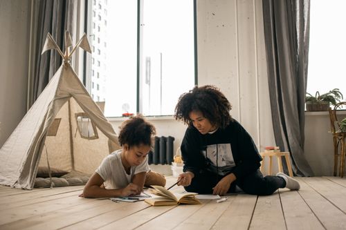 Free African American woman with Afro hairstyle doing homework with daughter lying on floor in kid bedroom Stock Photo
