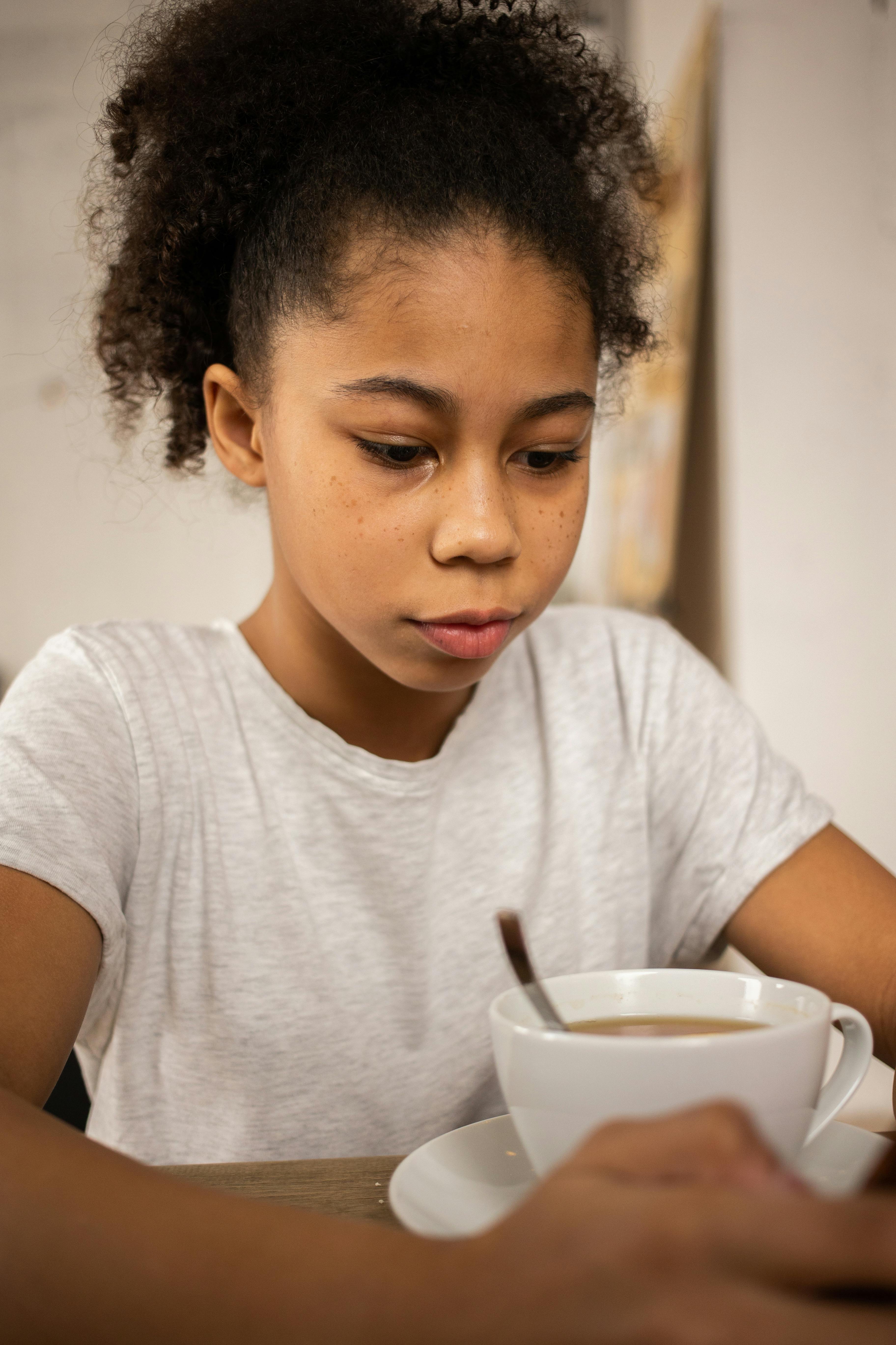 black girl using smartphone at table with cup of coffee