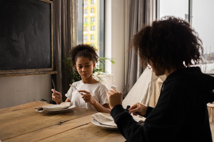 Black Girl With Unrecognizable Mother Learning Table Manners