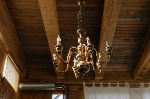 Free Elegant chandelier hanging from a rustic wooden ceiling, capturing a classic and antique interior decor. Stock Photo