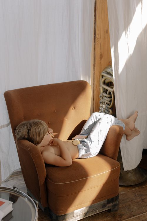 Free Boy lounging on a brown armchair in a warmly lit indoor setting. Stock Photo