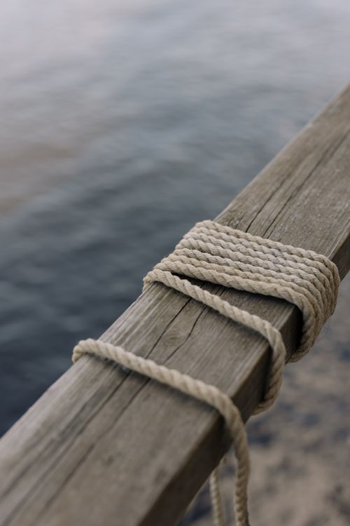 Free Detailed close-up of a rope tied on a weathered wooden post by the water Stock Photo