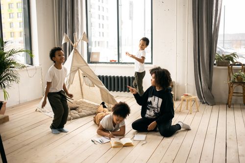 Free Full body of African American mother sitting on wooden floor near black kids playing in light room with blanket fort Stock Photo