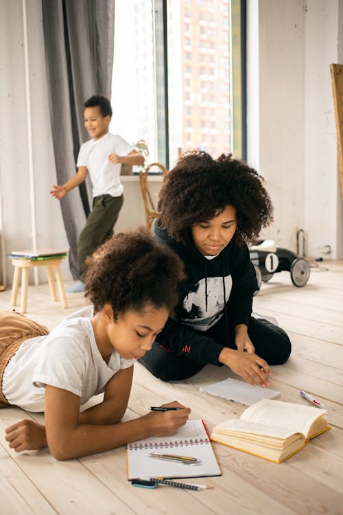 Focused black mother doing homework with daughter on floor