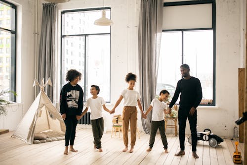 Full body of content African American parents with black kids standing together while spending time in light room with blanket fort