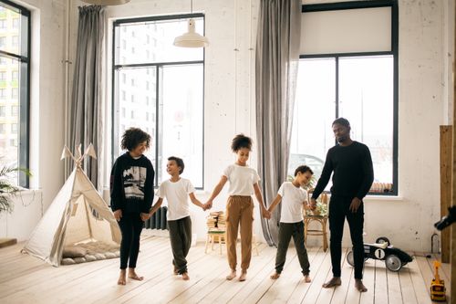 Free Full body of content African American parents with black kids standing together while spending time in light room with blanket fort Stock Photo