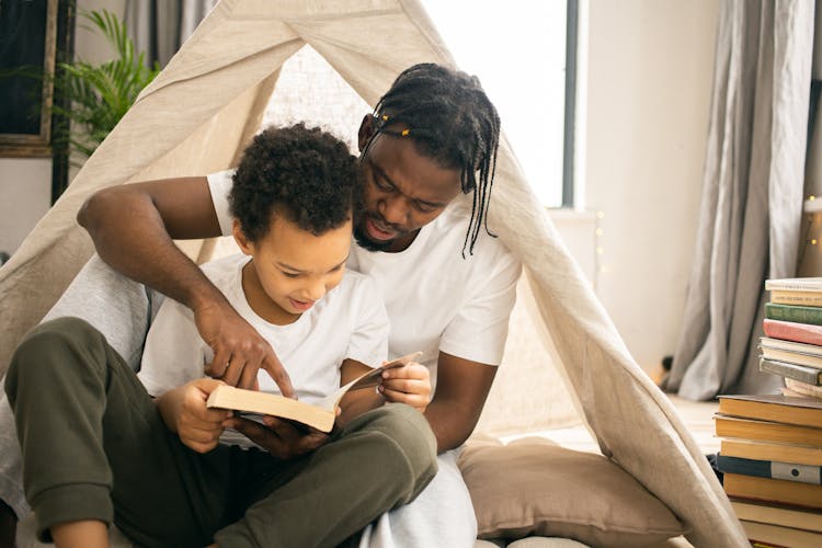 Concentrated Black Man Reading Book With Son At Home