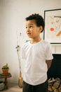 Shy little black child standing at home with hands behind back head