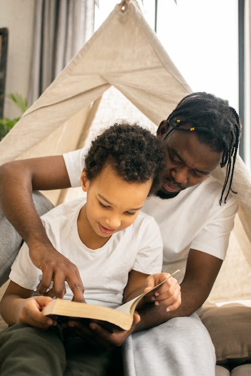 Free Happy black father and little son smiling and reading textbook together Stock Photo