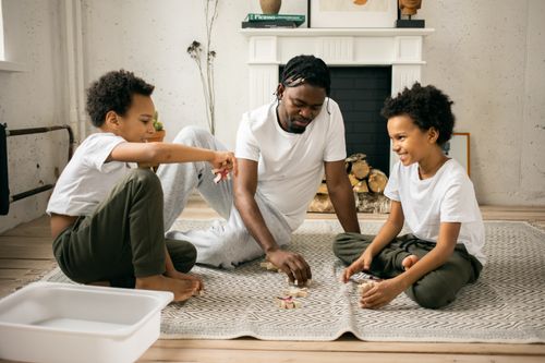 Free Full body of cheerful African American twin brothers in similar casual clothes smiling while sitting on floor and playing with toys together with happy young father Stock Photo