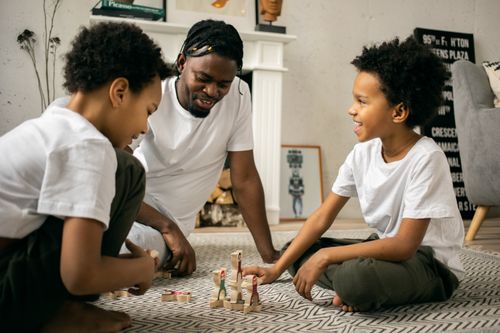 Free Positive African American father sitting on floor and playing with children with wooden figures in living room in daytime Stock Photo