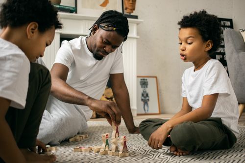 Free Concentrated African American father moving wooden figures while playing with children at home in daytime Stock Photo