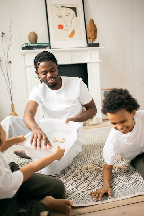 Free Cheerful African American father in casual clothes playing with laughing son in living room in daytime Stock Photo