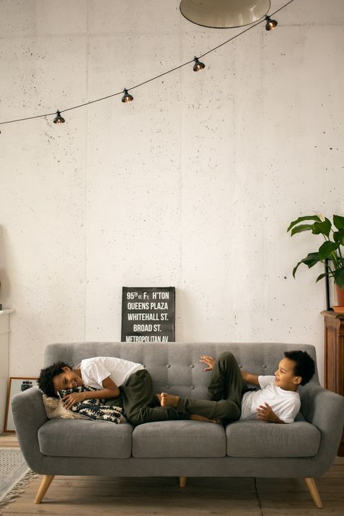 Free Side view of cheerful African American little brothers in casual clothes having fun on comfortable sofa in living room at home in daytime Stock Photo
