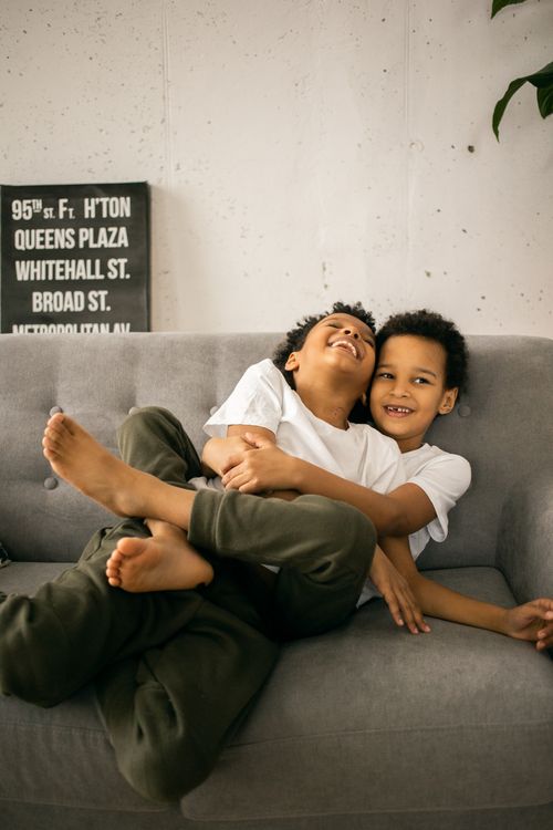 Free Cheerful African American brothers sitting on comfortable sofa and laughing while spending time at home in daytime Stock Photo