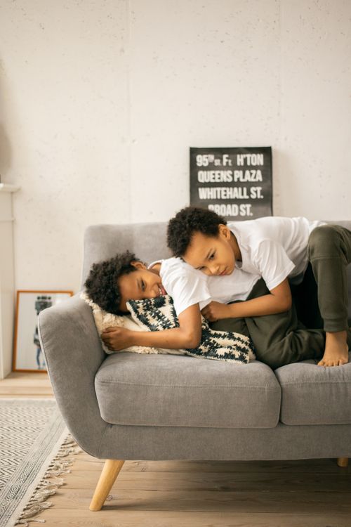 Free Positive African American brothers in casual clothes hugging and lying on comfortable sofa in light living room Stock Photo