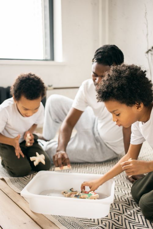 Free Calm African American father and sons sitting on floor and putting wooden figures in plastic container at home in daylight Stock Photo