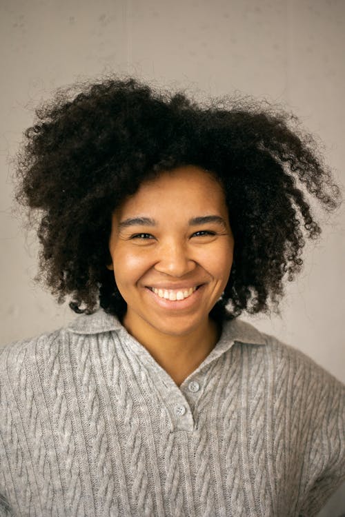 Free Cheerful African American woman with dark curly hair in casual clothes looking at camera against light background Stock Photo